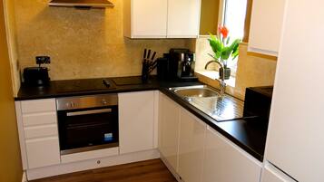 A compact kitchen with white cabinets, a built-in oven, a coffee machine, and a sink.