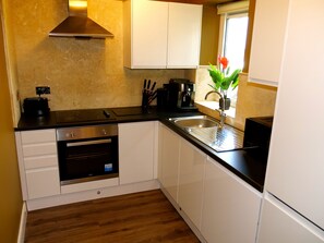 A compact kitchen with white cabinets, a built-in oven, a coffee machine, and a sink.