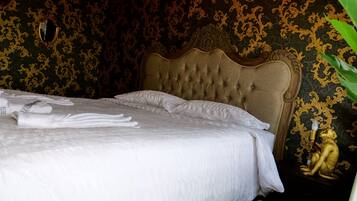Una cama bien hecha con ropa de cama y toallas blancas, un cabecero capitonado y una estatua dorada sobre una mesita de noche.