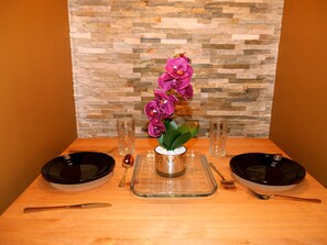 A dining table set with two black plates, a clear glass pitcher, a spoon, and a fork. A vase with purple flowers is centered on the table. - Deluxe Versace Styled Apartment (South Yorkshire)