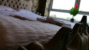 A bed with a tufted headboard, a neatly made bed with pillows and a blanket, and a window with a view of greenery outside.