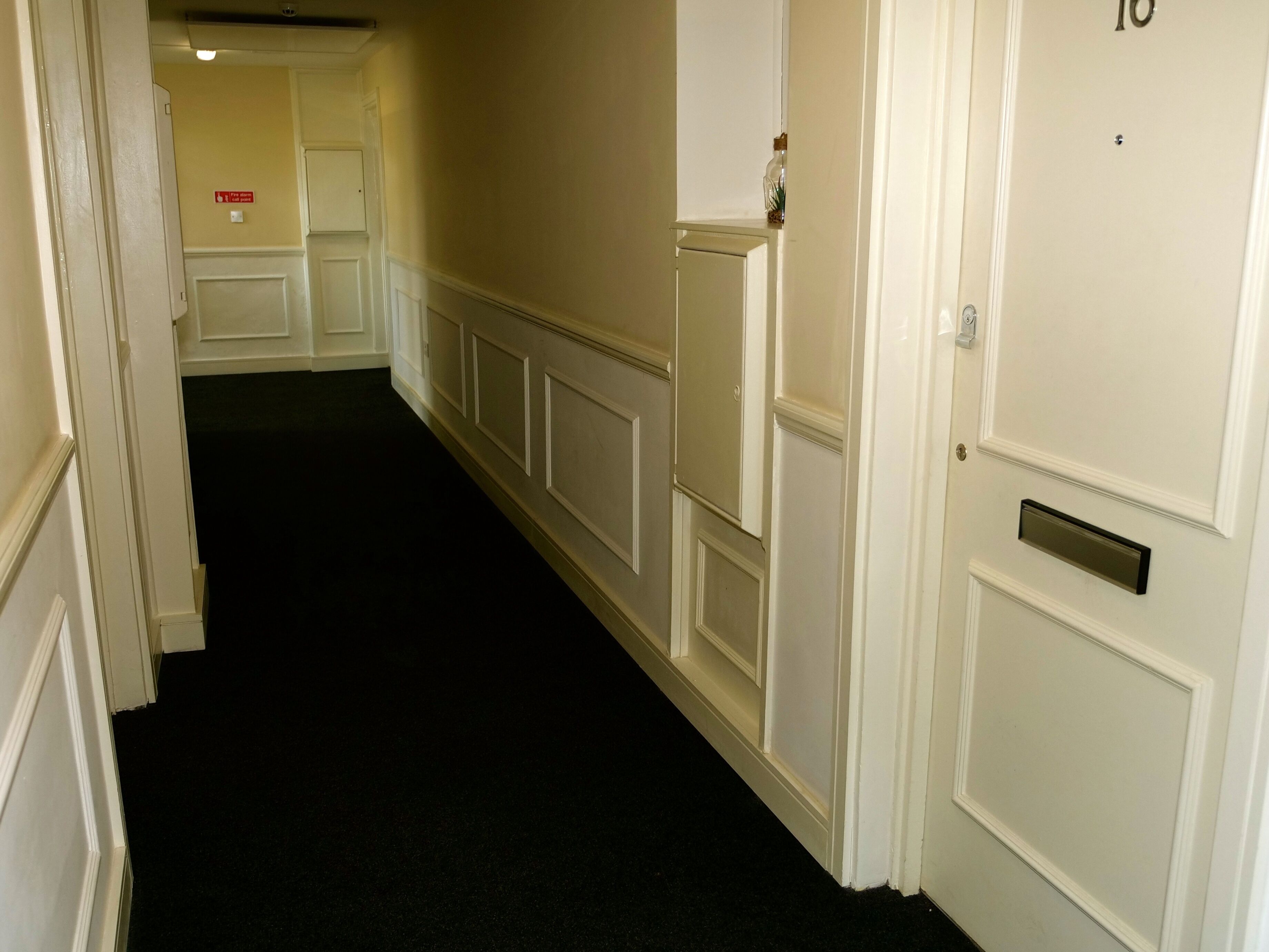 A hallway with white walls and doors, including a door with a number plate.
