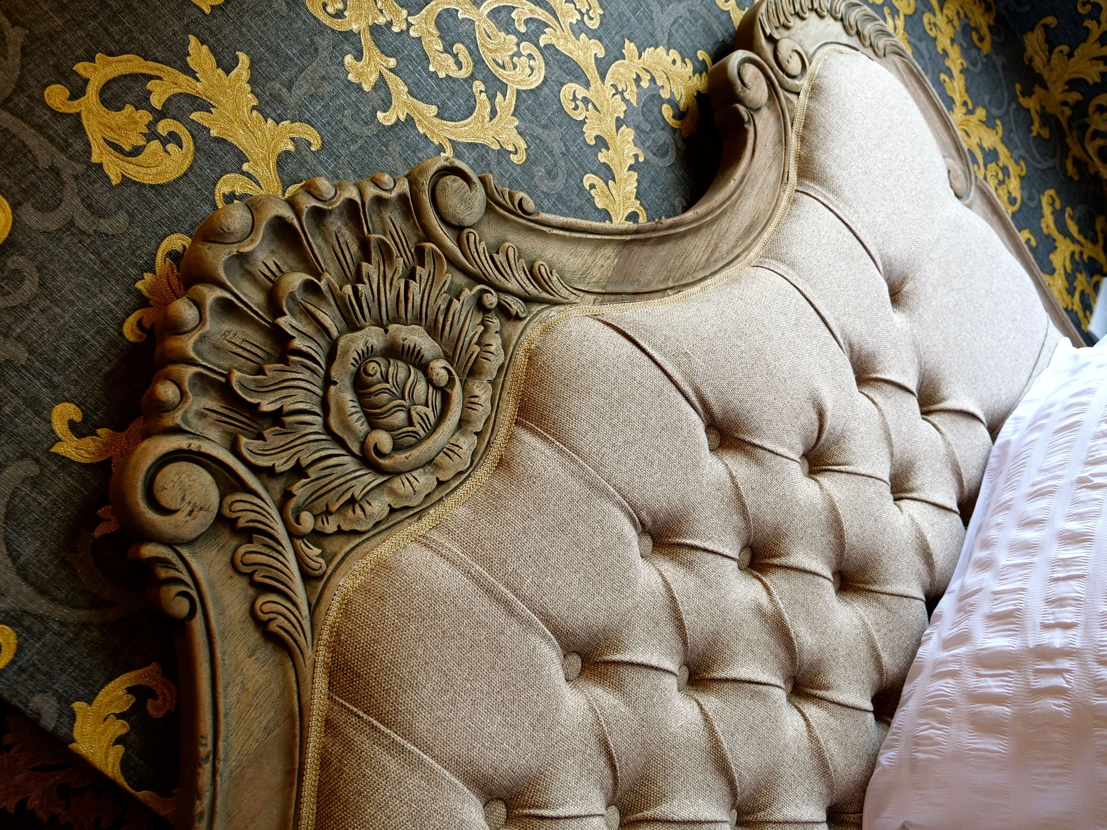 Une tête de lit capitonnée, ornée de sculptures complexes et dotée d’un fond en tissu à motifs.