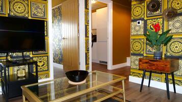 A living room with a glass coffee table, a flat-screen TV, a wooden side table, and a decorative vase with flowers.