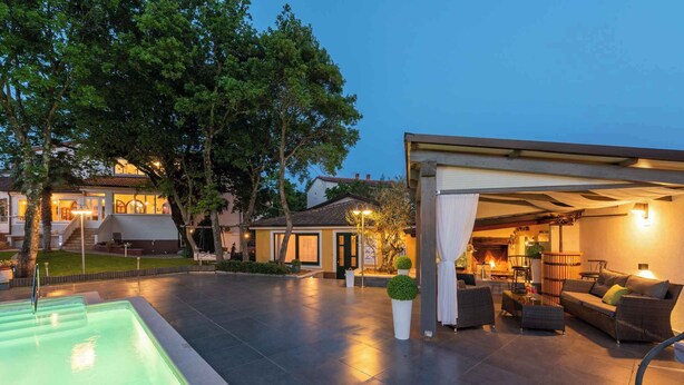 Un espacio al aire libre techado con piscina, mobiliario y un edificio con iluminación cálida.