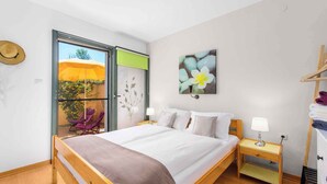 Un dormitorio con cama, mesitas de noche, armario, ventana con vistas a un área exterior y una obra de arte colgada en la pared.