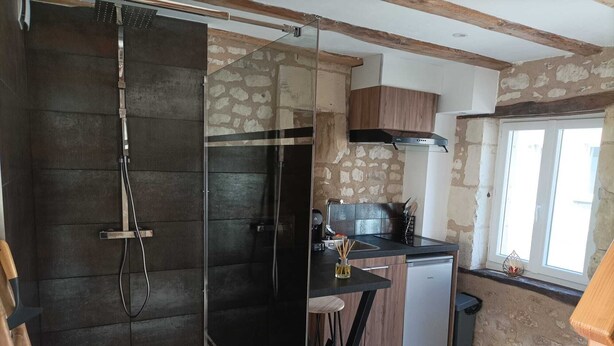 A compact kitchen with a stone wall, a wooden ceiling, and a small bar stool. - L'instant Civray (Civray sur esves)