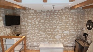 A living room with exposed stone walls, a white bench, a wooden coffee table, a sofa, and a TV mounted on the wall. - L'instant Civray (Civray sur esves)