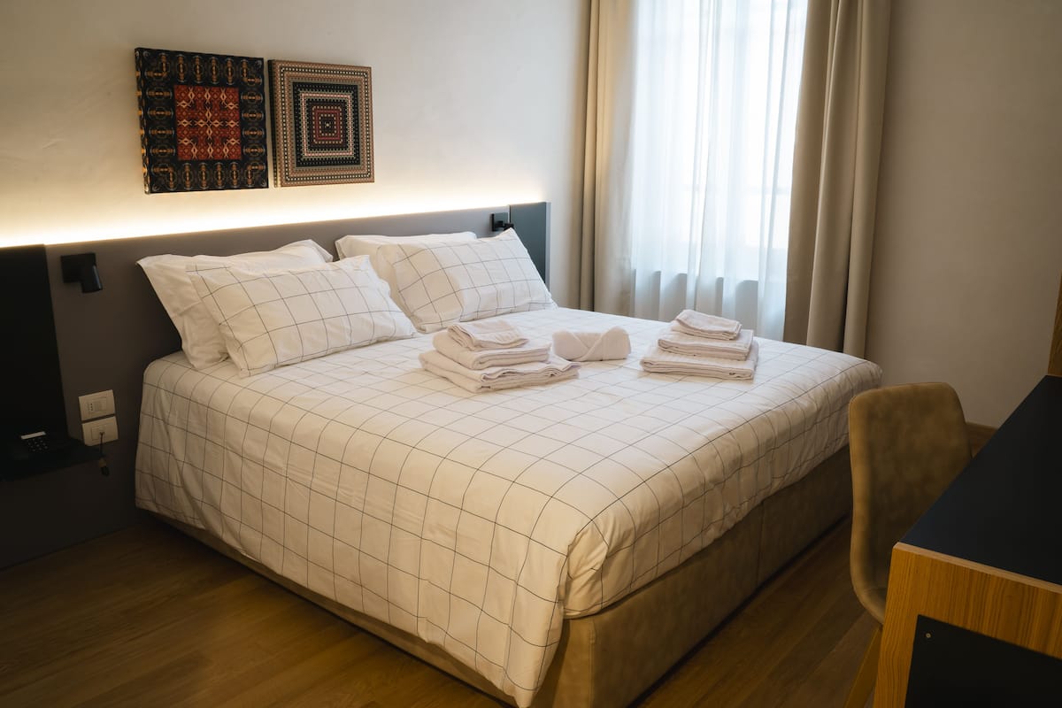 Cama bem arrumada com colcha de padrão quadriculado, mesa de cabeceira e uma cadeira.