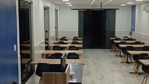Una sala de conferències moderna amb sòcols de marbre, escriptoris de fusta i cadires negres.