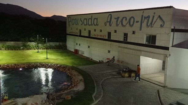 Un edifici amb un rètol que diu "Pousada Arco-fis" i una zona enjardinada amb un estany i gespa.