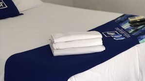 Un llit ben fet amb llençols blancs i una manta blava, una petita planta en test i alguns comandaments a distància sobre el llit.