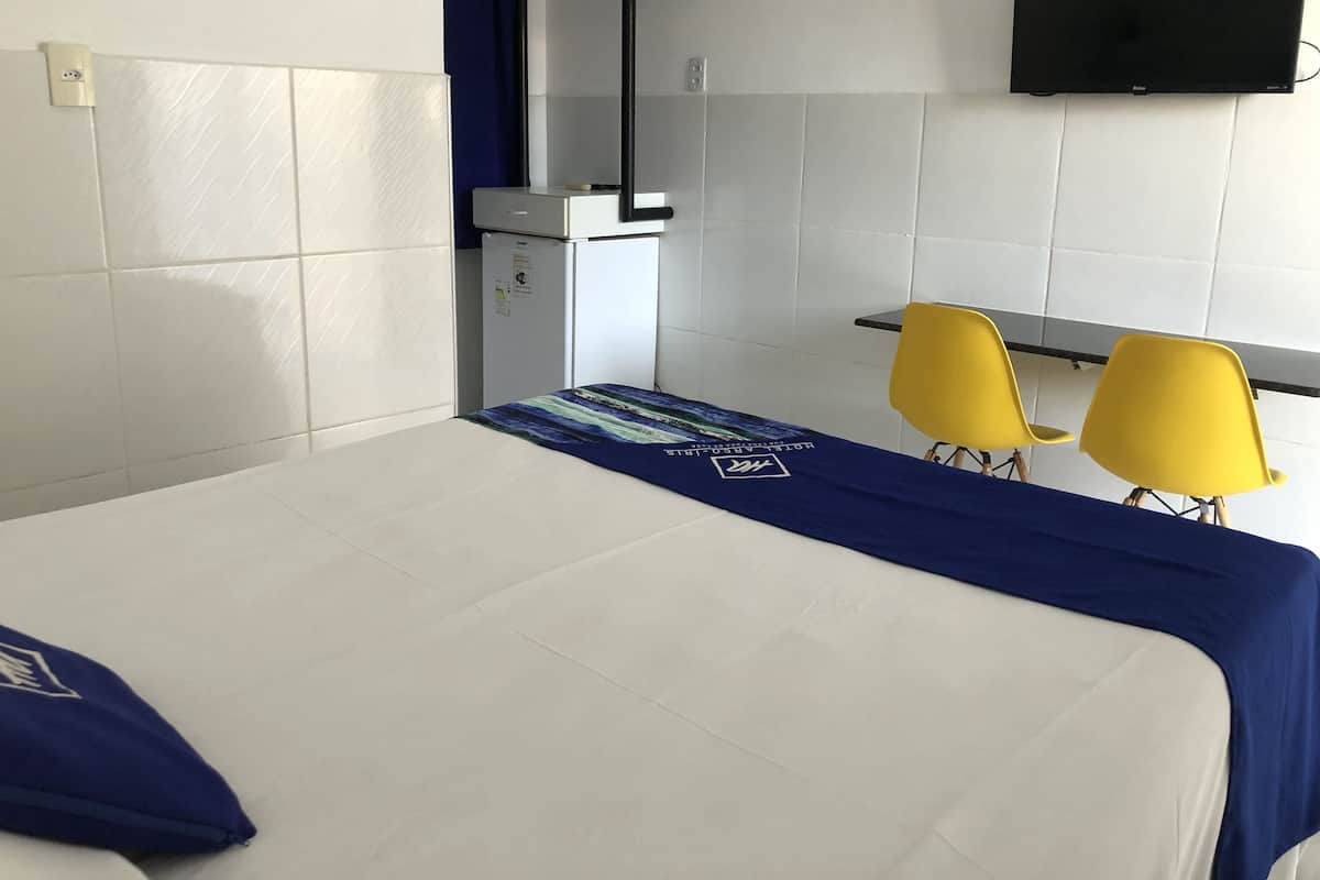 Habitación de hotel con cama, escritorio, dos sillas amarillas, televisor en la pared y un refrigerador pequeño.
