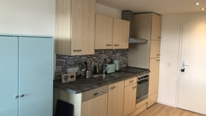 A modern kitchen with light wood cabinets, a stone backsplash, and a built-in oven.