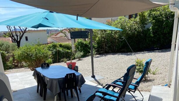 An outdoor patio area with a table and chairs, covered by a large umbrella.