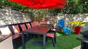 An outdoor patio with a stone wall, a wooden table, and a blue chair.