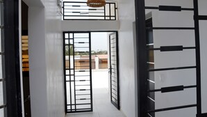 Un couloir avec une grille en métal noir, un luminaire au plafond et une vue sur les bâtiments à l’extérieur.