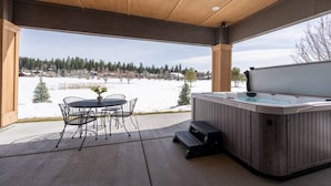 Eine überdachte Terrasse mit Whirlpool, Gartenmöbeln und Blick auf eine verschneite Landschaft.