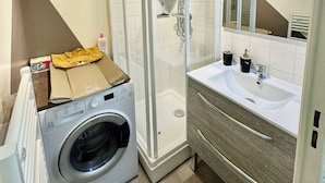 Un bagno moderno con doccia vetro, lavatrice integrata, un ampio lavabo con specchio e un porta asciugamani.