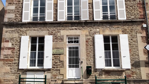 A two-story stone building with white shutters, a central door with a barred window, and a sign reading "Gite de Montfort". - Gîte de Groupes de 2 à 12 Personnes (Guillon-Terre-Plaine)