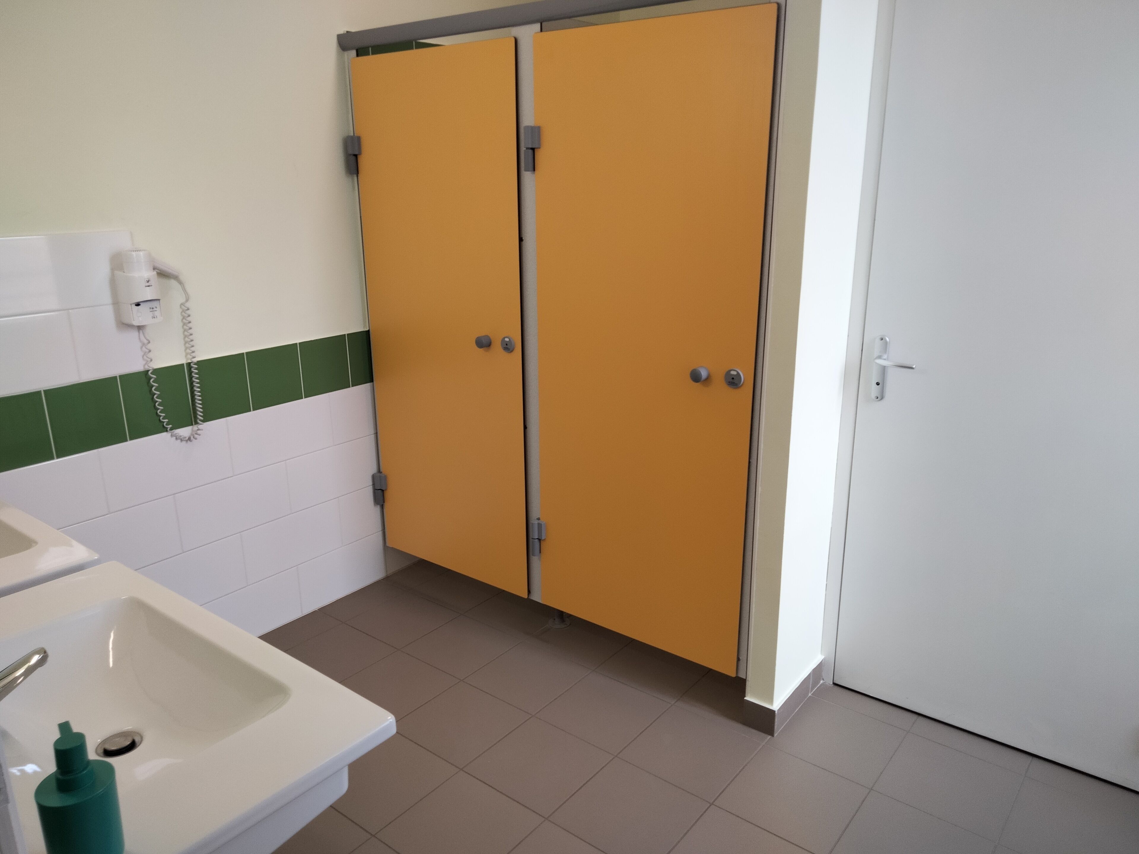 A bathroom with a white sink, green and white tiled walls, and two yellow doors.