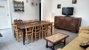 A dining area with a wooden table and chairs, a television on a wooden cabinet, and a beige sofa. - Gîte de Groupes de 2 à 12 Personnes (Guillon-Terre-Plaine)