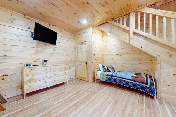 Une chambre rustique en bois, avec un lit, un bureau et un téléviseur fixé au mur.
