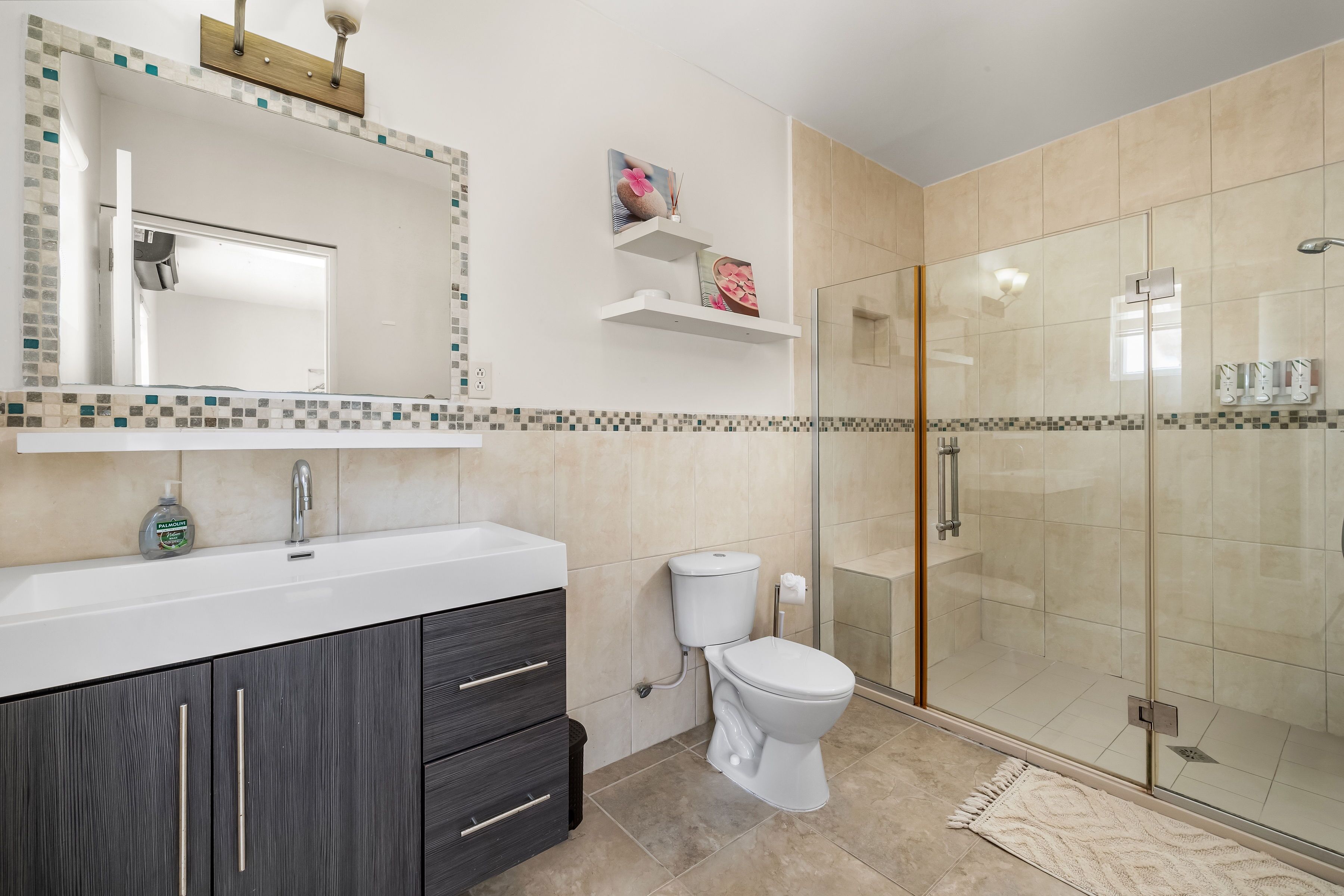Een moderne badkamer met een douchecabine van glas, een wit wastafelmeubel met donkere kast en een toilet.
