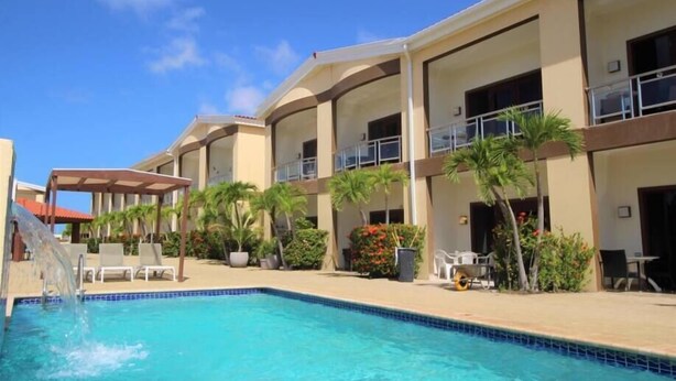 Un hotel con piscina, mobiliario exterior y palmeras.