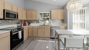 Une cuisine moderne avec des meubles de couleur bois clair, un four à micro-ondes en acier inoxydable, une cuisinière à gaz et un lave-vaisselle.