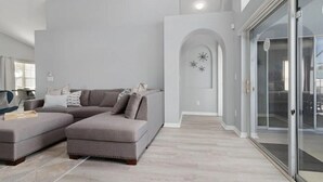 Un salon moderne avec un canapé d’angle, une porte vitrée donnant sur un balcon et un design minimaliste.
