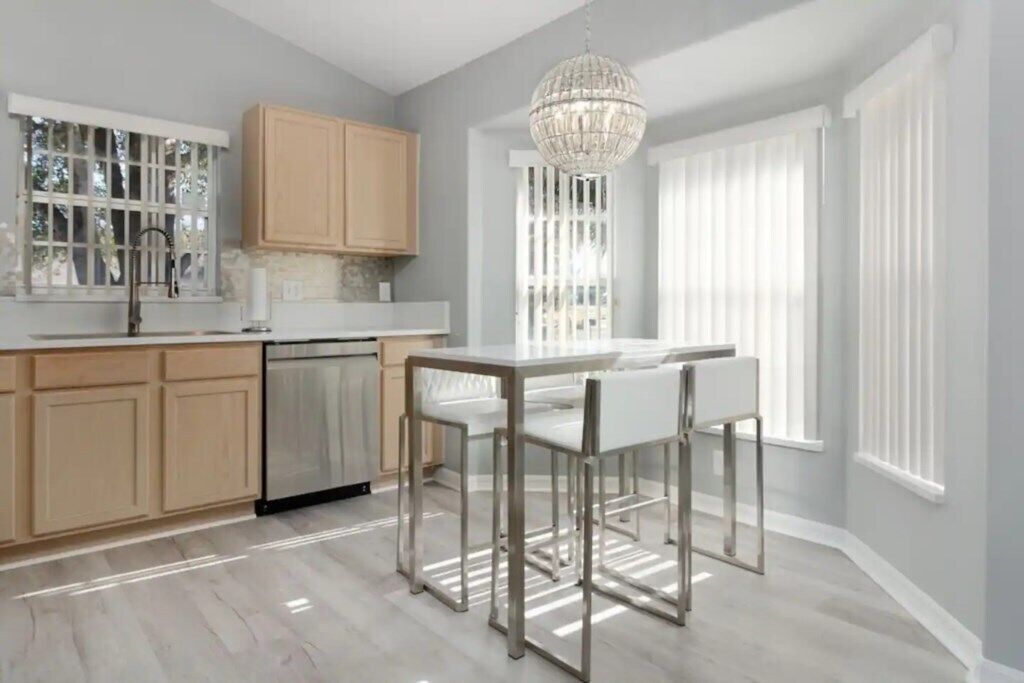 A modern kitchen with a dining area, featuring a chandelier, wooden cabinets, and a view of the outdoors.