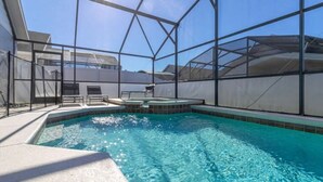 Une piscine dotée d’une enceinte en verre, entourée d’une terrasse blanche et d’une clôture en métal.