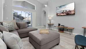 Un salon moderne avec un canapé d’angle gris, une table basse en bois et un tableau représentant une scène de plage.