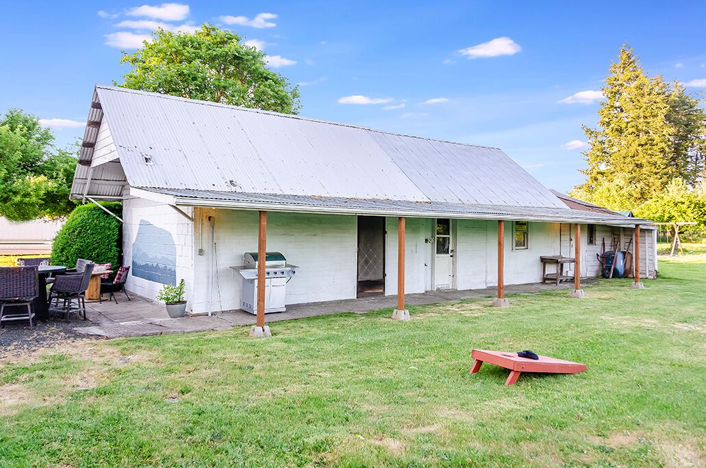 A single-story building with a metal roof, a covered porch, and a barbecue grill in the front yard.