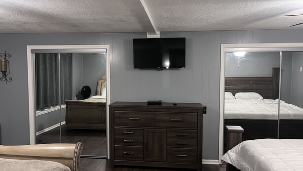 A bedroom with a bed, a dresser, a mirror, a television, and a closet.
