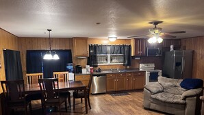 A compact kitchen with wooden cabinets, a dining table with chairs, a built-in oven, and a ceiling fan.