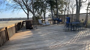 A wooden deck with a railing, outdoor furniture, and a view of a field.