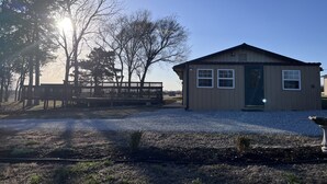 A small, single-story building with a gabled roof and a front door, surrounded by a gravel driveway and a wooden fence.