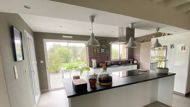 A modern kitchen with a large island, pendant lights, and a view of the garden.