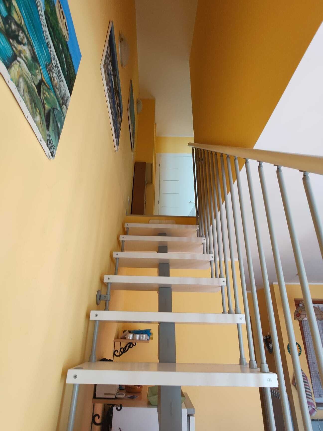 A staircase with a metal railing, a white door at the top, and a yellow wall with a painting.