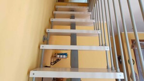 Una escalera con barandilla de metal, una puerta blanca en la parte superior y una pared amarilla con un cuadro.