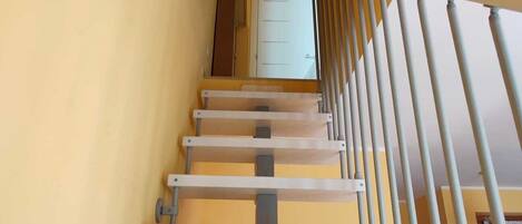 A staircase with a metal railing, a white door at the top, and a yellow wall with a painting.