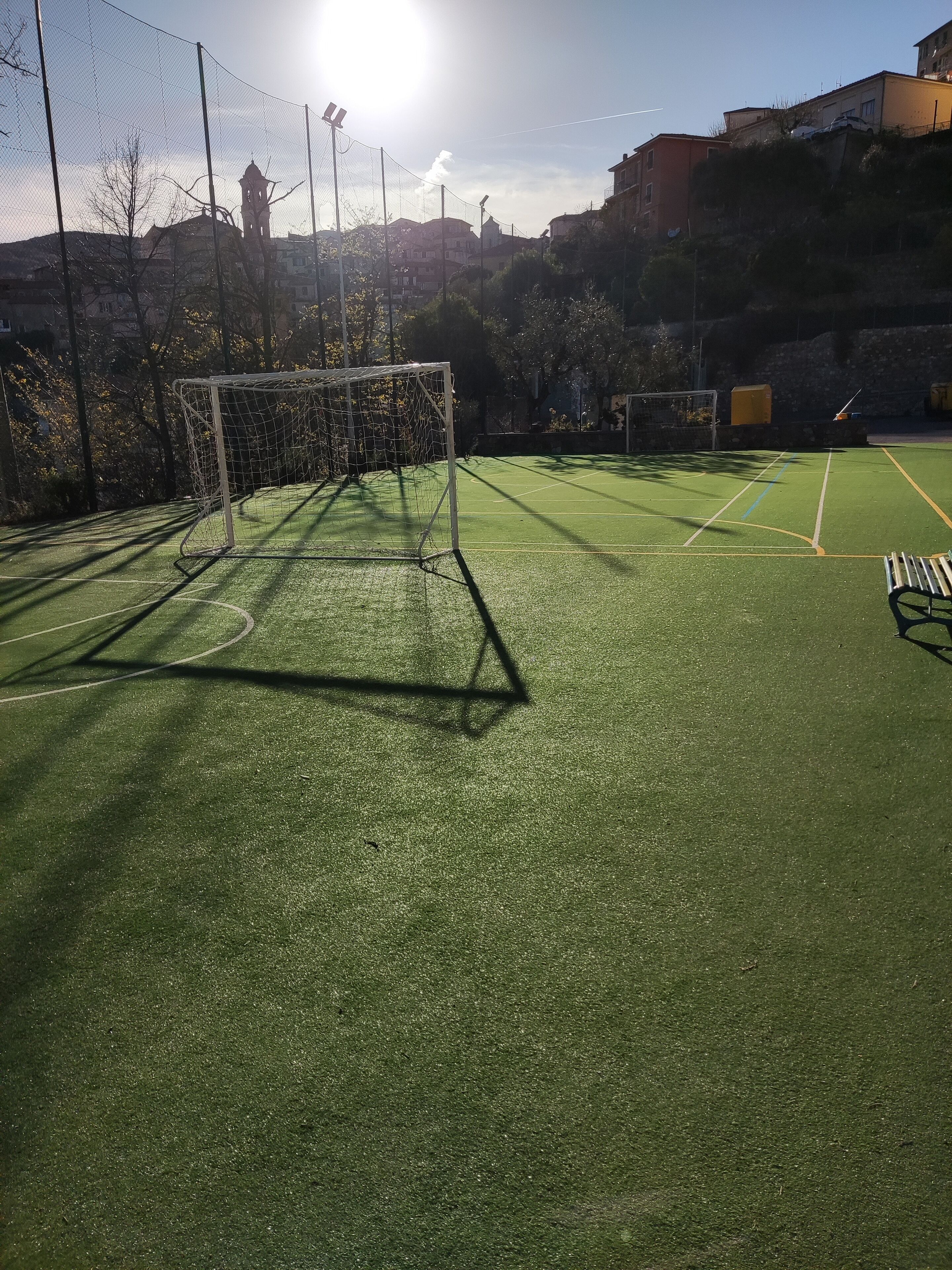 A soccer field with a goalpost, surrounded by a fence, and buildings in the background.