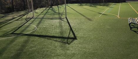 A soccer field with a goalpost, surrounded by a fence, and buildings in the background.
