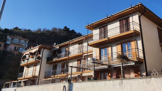 Un edificio de varios pisos con balcones, base de piedra y un cielo azul despejado.