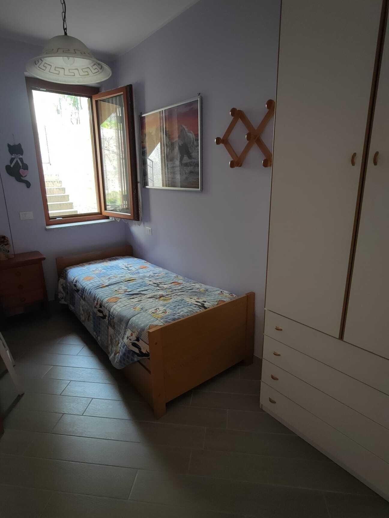 Un dormitorio con cama, armario, ventana y lámpara colgante.