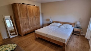 Un dormitorio con cama de madera, mesitas de noche, armario y ventana con cortinas.