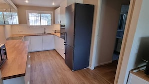 Cocina compacta con encimera de madera, armarios blancos, refrigerador negro y ventana que proporciona luz natural.
