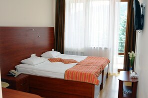 A hotel room with a wooden bed, white bedding, a striped blanket, a bedside table with a phone, and a window with curtains.